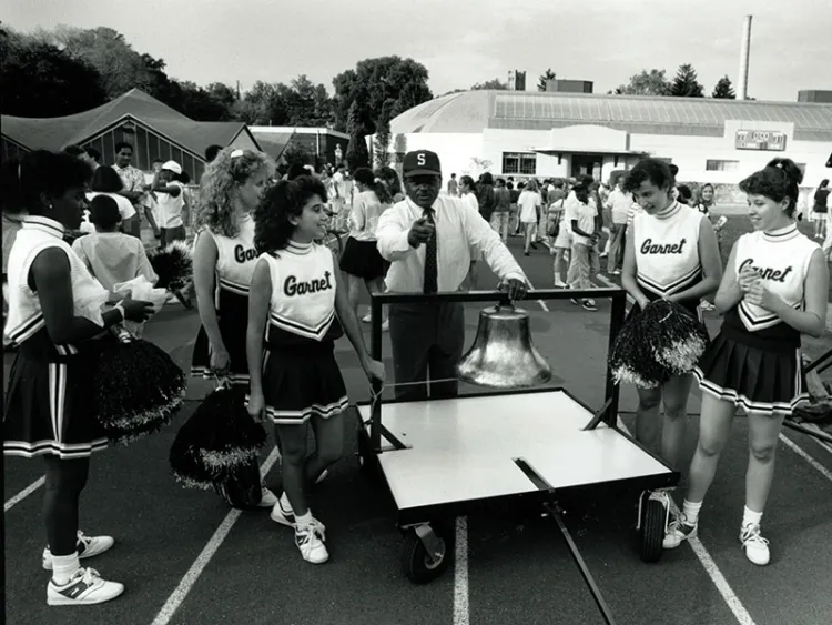 Robert Williams with bell and Garnet cheerleaders on clothier track