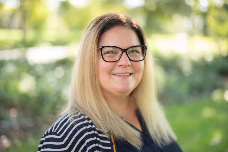 Woman in glasses outside with leaves and grass in background.