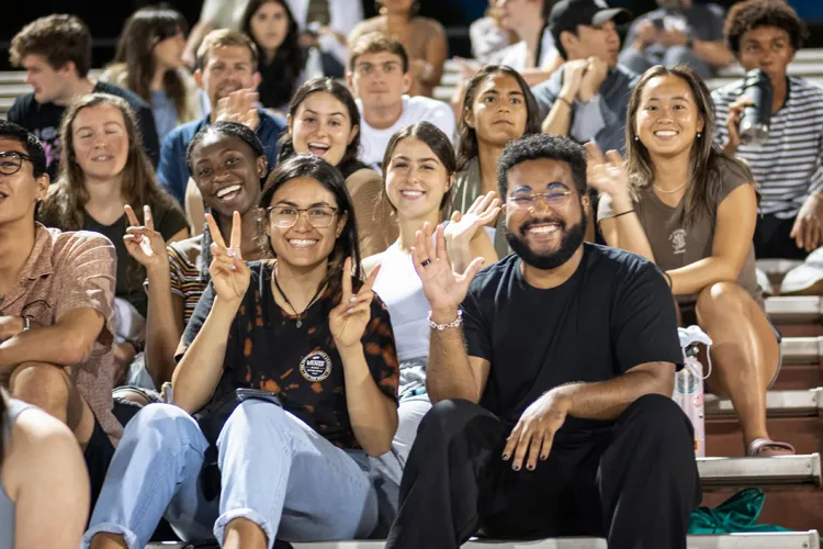 Students sit in bleachers at night