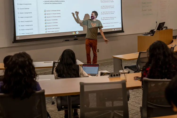 Professor wearing masks gestures at projector screen