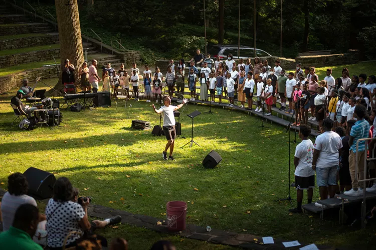 Person stands in outdoor amphitheater conducting choir