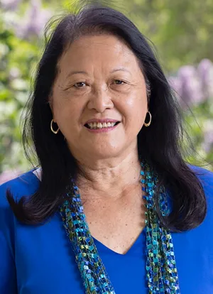 Amy Cheng Vollmer in blue top standing outside in front of blooming flowers
