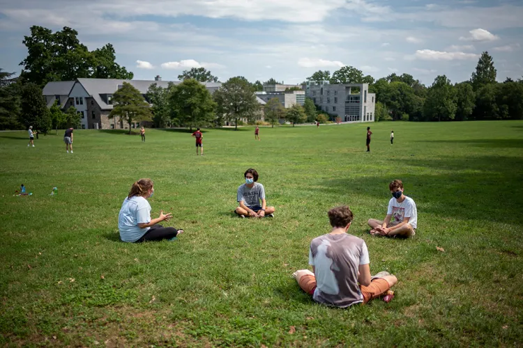 Students sit on grass near Mertz during summer. A few clouds in the sky.