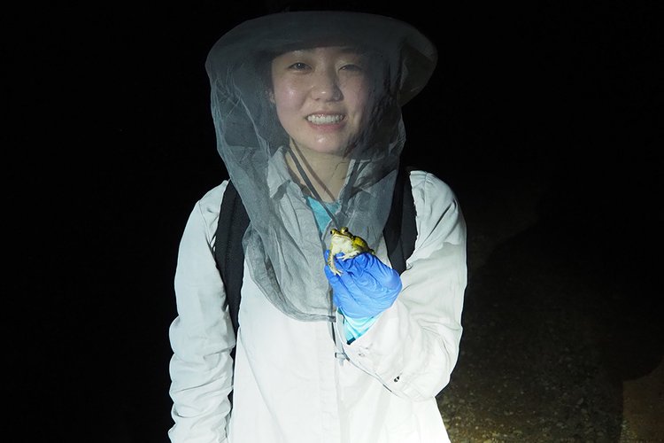 Student standing outside at night holds a frog
