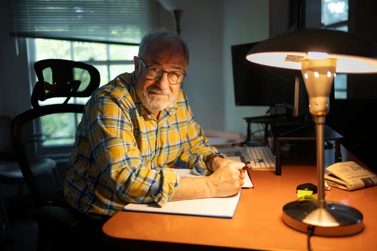 Ted Gup sits next to lamp sitting at desk