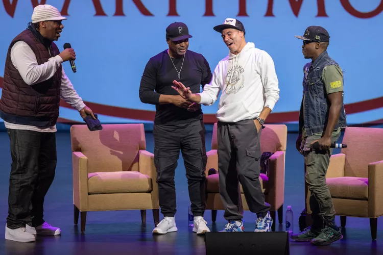 Group of rappers talk onstage with Swarthmore logo partially obscured on projection behind them