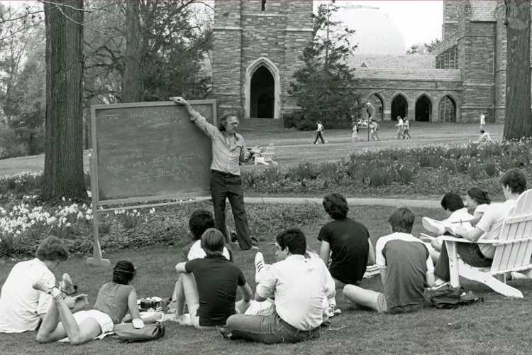 Gene Klotz teaches outdoor on blackboard with clothier bell tower in background