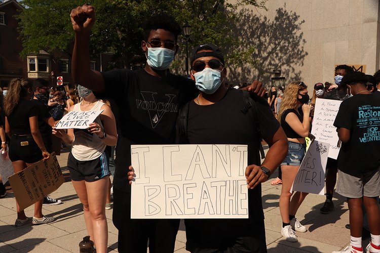 Two young men wearing black shirts with raised fist and a shirt that says "I Can't Breathe".