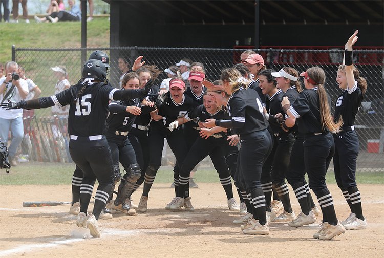 Softball team stands at home plate celebrating home run by Kate Hart
