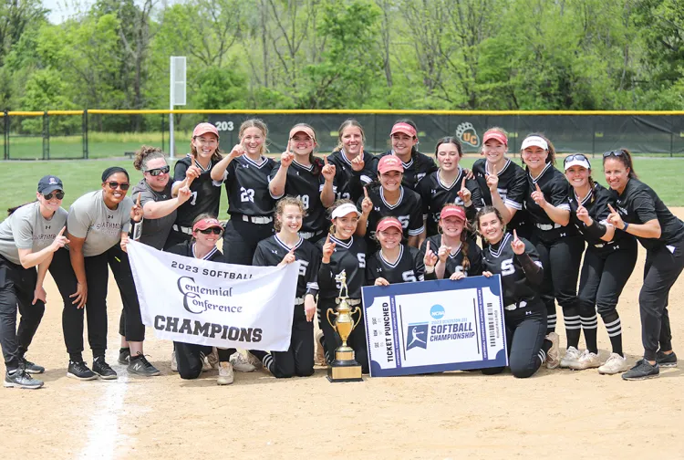 Softball team poses with conference trophy on field