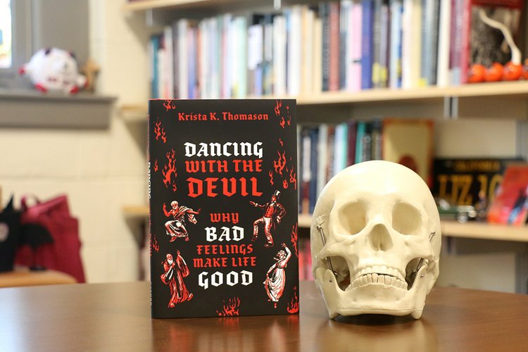Skull on table with book entitled "Dancing with the Devil"