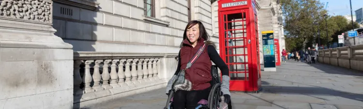 Young woman uses a wheelchair on a British street with a classic red phone booth in backdrop.