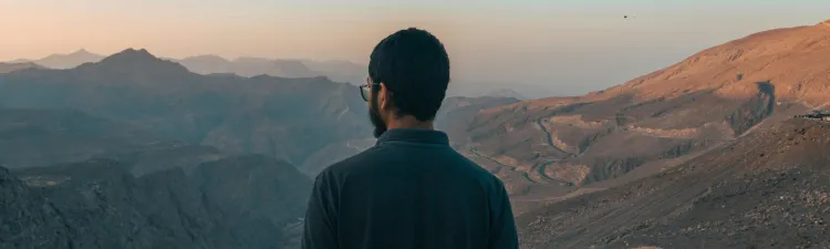 Dark haired male wearing polo shirt stands facing canyon with his back to the camera