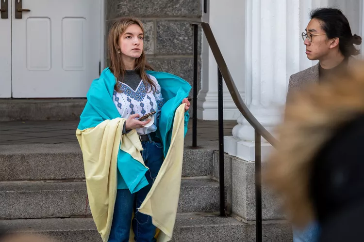 Person wrapped in Ukrainian flag stands in front of building