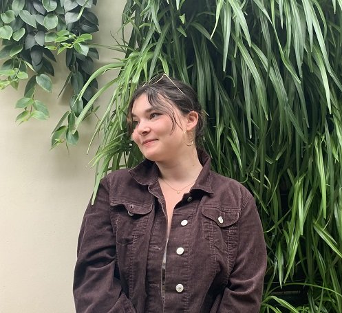 student sitting and smiling in front of wall of plants