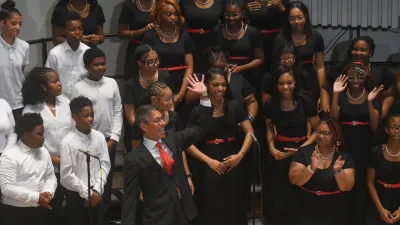 John Alston stands in front of a children's choir on stage clapping 