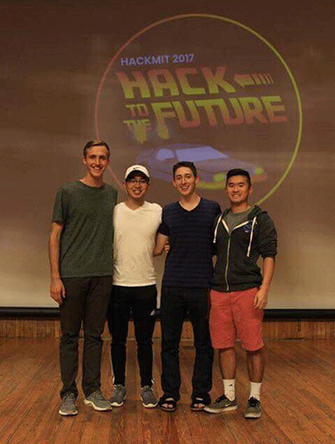 The four members of the hackathon team stand together in front of the event's logo