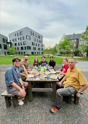 Photo of group of student and faculty sitting around an outdoor picnic table in a courtyard