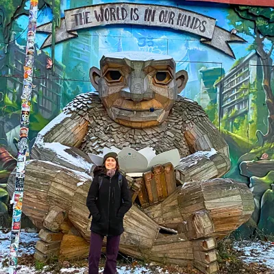 Female student stands in front of large statue of troll beneath mural stating the world is in our hands