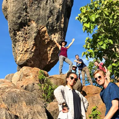 Four students stand next to balancing rock with blue skies