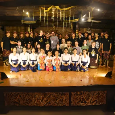 Swarthmore students kneel alongside a large assembly of Gamelan performers kneel on a stage. 