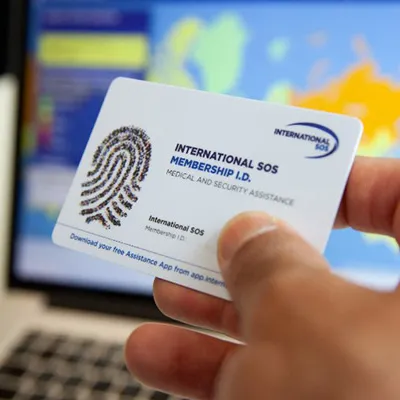 Hand holds an ISOS membership id card in front of an open laptop showing a map