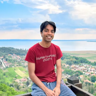 Student wearing red Swarthmore tshirt sits on wood railing in front of European overlook