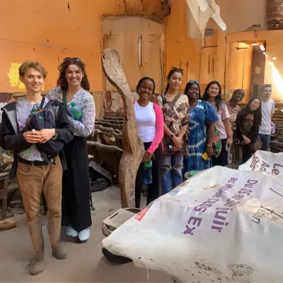 Group of students stands in an arts workshop in front of a yellow wall.