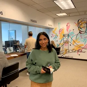 Female student stands in consular office with mural on white wall holding her passport