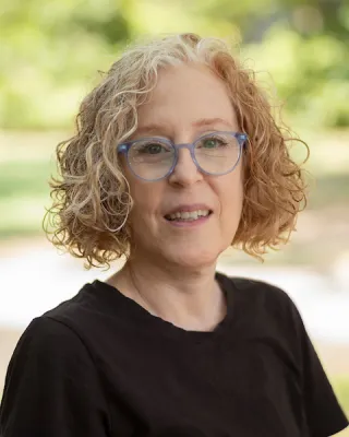 Woman with short curly hair and glasses smiles at the camera.