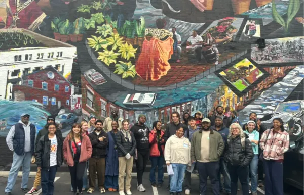 Image of a large group of people standing under a mural depicting a city street with people on it