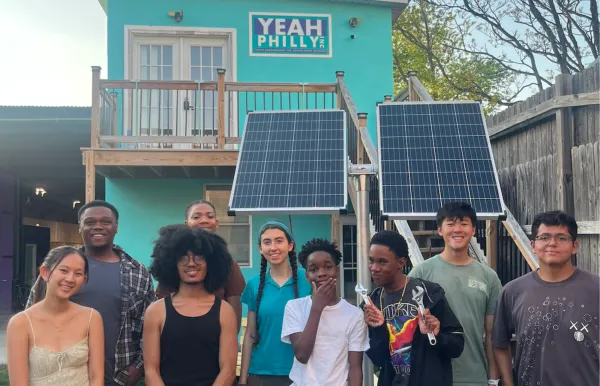 Image of students standing in front of a turquoise house with solar panels that says YEAH Philly Inc. on it.