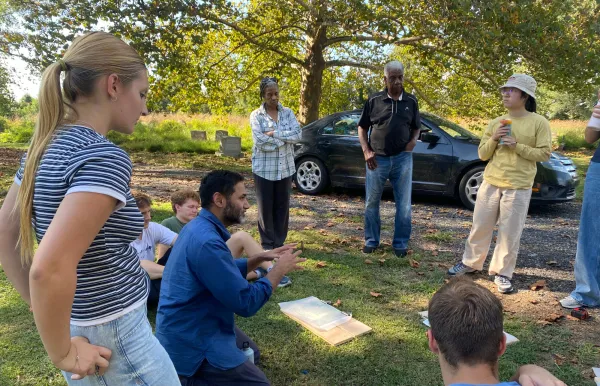 Image of students and community partners gathered round as a professor speaks at a local Chester cemetery called Green Lawn Cemetery