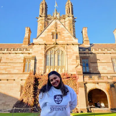 Student in University of Sydney Sweatshirt stands in front of academic building