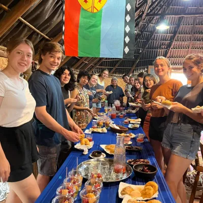 Students stand on both sides of a long table in a wicker structure