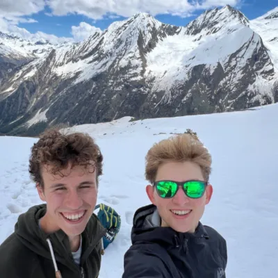 Two male students stand in snowy setting with alpine mountains in background