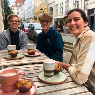 3 students sit sipping coffee at a streetside cafe