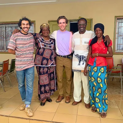 Two students stand with local program staff on a tile porch in Cameroon
