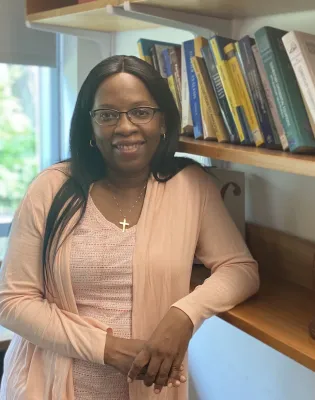 Nsoki posing in front of a bookshelf and smiling