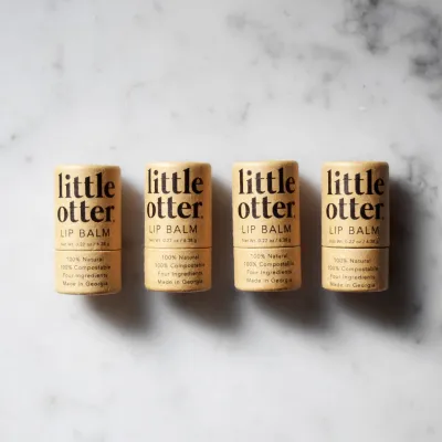 The image depicts 4 carboard tubes of lip balm with the brand 'Little Otter" written across the front, along with the flavor of lip balm