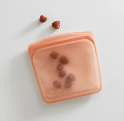 This image depicts a pink/orange silicon bag with a few nuts inside and a few nuts on the surface next to it, as if to show they spilled out a bit