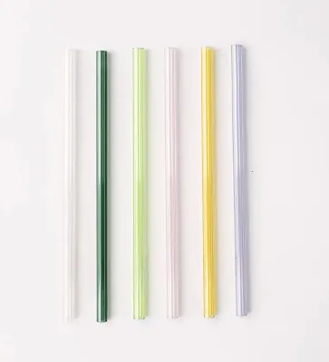The image depicts five glass straws in a variety of colors standing parallel in al ine