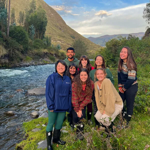 Group of students stands next to river with mountain behind them.