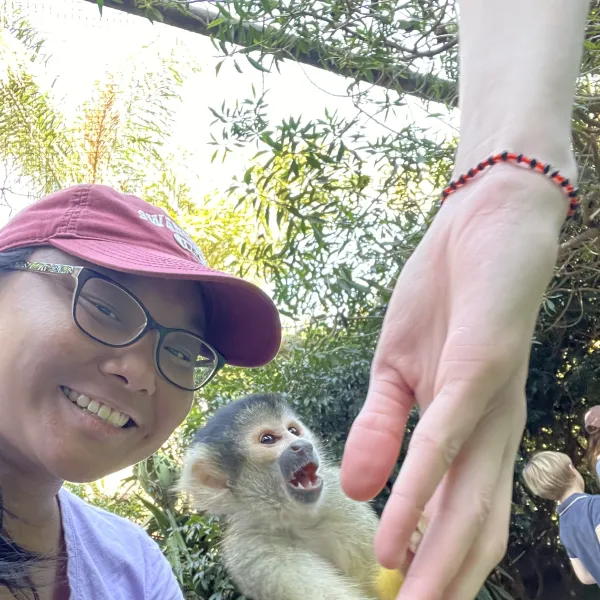 Female student next to spider monkey holding another student's finger