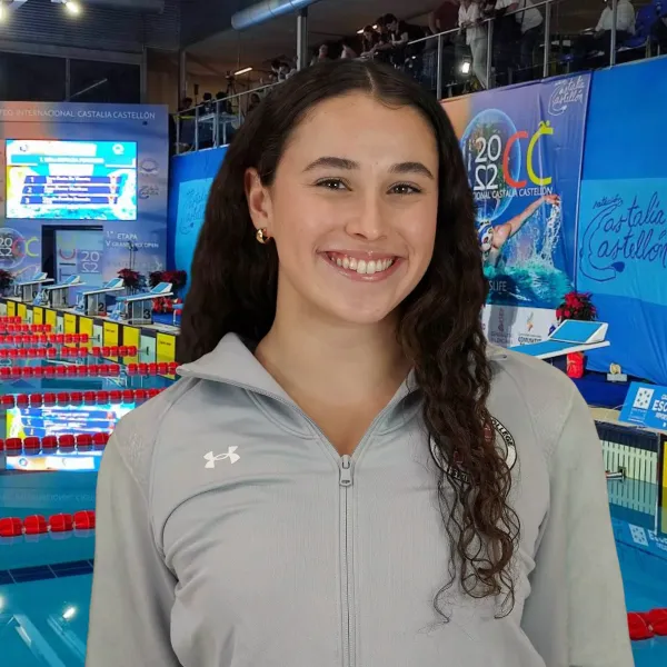 Female student smiles in front of olympic sized swimming pool