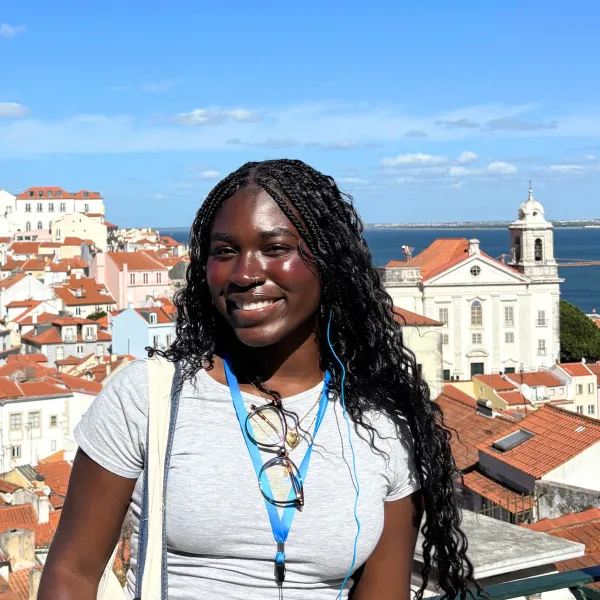 Student smiles in front of sunny Lisbon skyline.
