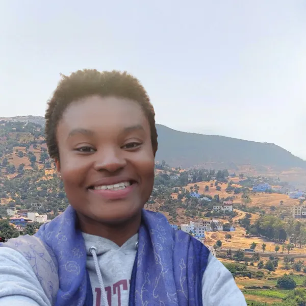 Female students stands smiling in front of hillside covered with houses.