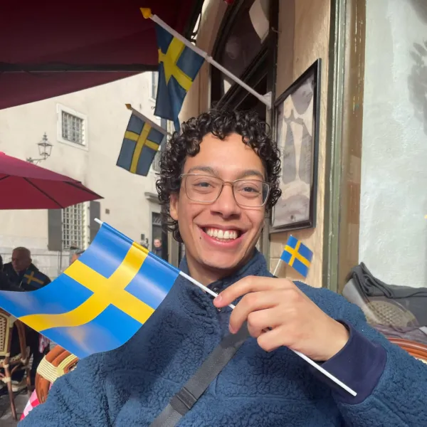 Male student in blue fleece waves miniature Swedish flag while seated