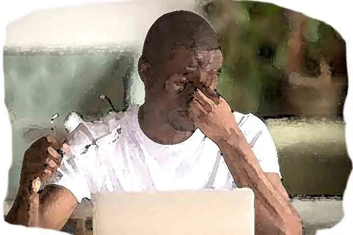 young man, sitting in front of computer, rubbing tired eyes