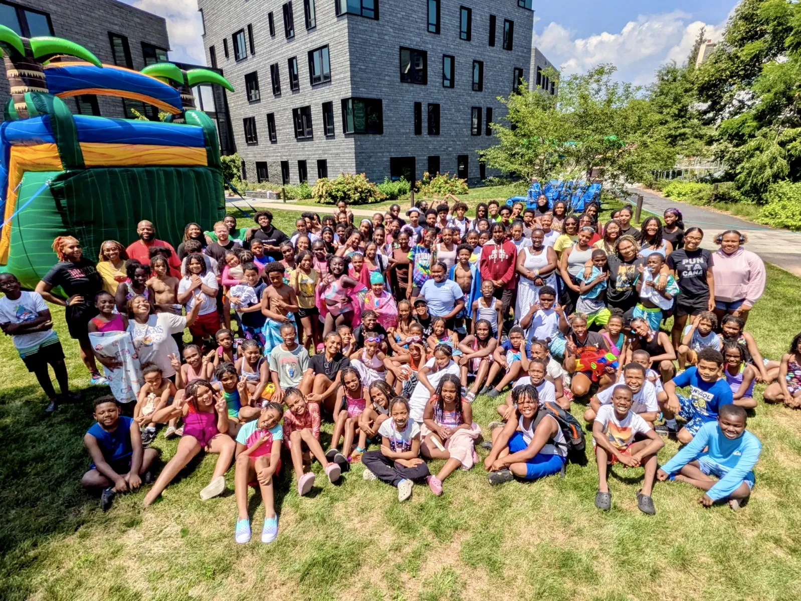 a large group of children, more than 100, pose for a photo outside in the summer